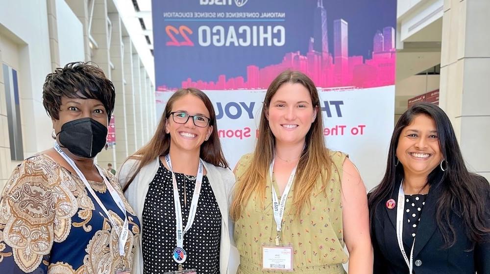 四个女人, 所有芝加哥十大彩票网赌CSME代表, 站在全国科学教学协会大会的横幅前.